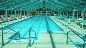 A large indoor swimming pool with a glass ceiling, surrounded by lounge chairs and a sunshade structure. - Perfect Vacation Getaway! Beach Condo in Quiet Setting, CLOSE TO THE BEACH! (Myrtle Beach)