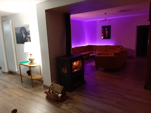 Een woonkamer met een houtkachel, een bank en een tafel met een lamp.