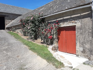 Een gebouw van steen met een rode deur en een tuin vol rode bloemen.