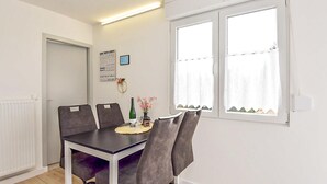 A dining area with a table and chairs, a window with curtains, a radiator, and a wall with a framed poster. - Cozy home in Goldlauter-Heidersbach (Goldlauter-Heidersbach)