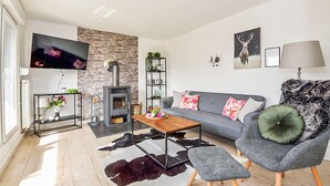 A modern living room with a stone wall, a fireplace, a grey sofa, and a television mounted on the wall. - Cozy home in Goldlauter-Heidersbach (Goldlauter-Heidersbach)