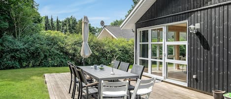 An outdoor patio with a wooden deck, a table with chairs, and a large umbrella.