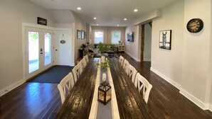 A spacious dining area with a long wooden table and white chairs, a cozy living room with a sofa and a TV, and a hallway with a wooden floor and a door. - Downtown -  Spacious Open Floor plan & Huge Kitchen Perfect for Family & Friend  (Saratoga Springs)