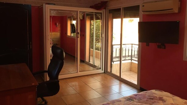 Een slaapkamer met een bed, een bureau, een stoel, een schuifdeur naar een balkon en een airconditioning op de muur.