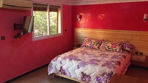 Een slaapkamer met een houten bed, bloemenbeddengoed, een rode wand en een raam.