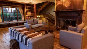 A cozy living room with a fireplace, a staircase, and a large window overlooking greenery. - Stunning View of San Jose-private property on 2 acres, Casa Los Cielos & Studio  (Mata de Plátano)