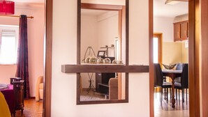 A room with a large mirror, a wooden shelf with decorative items, a dining area with chairs, and a view into another room. - Fonte da Rosa Guest House APT2 (Belmonte)