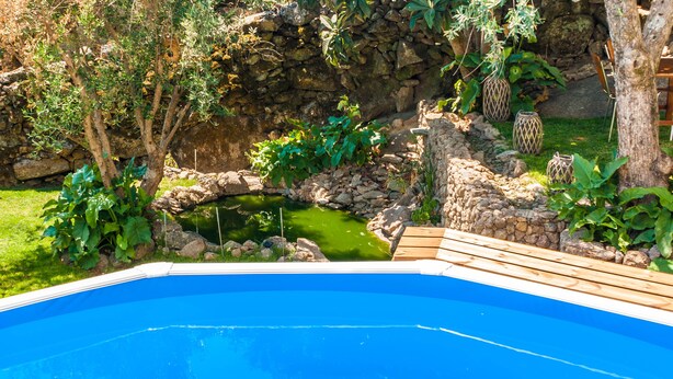 A swimming pool with a wooden deck, surrounded by greenery and a stone wall. - Fonte da Rosa Guest House APT2 (Belmonte)