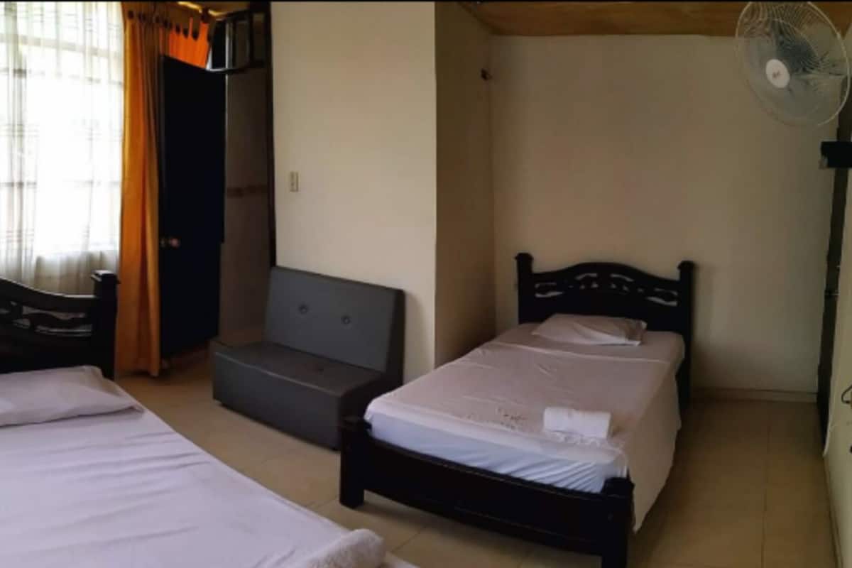 A room with two single beds, a small sofa, and a standing fan.