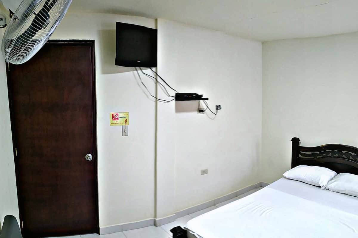 A bedroom with a bed, a TV mounted on the wall, a door, and a wall socket.