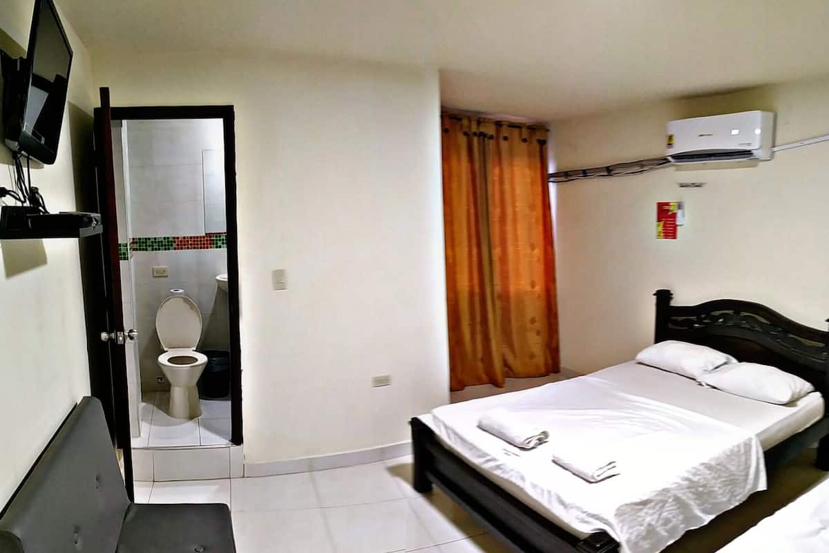 A bedroom with a bed, a television, an air conditioner, and a bathroom with a toilet and shower.