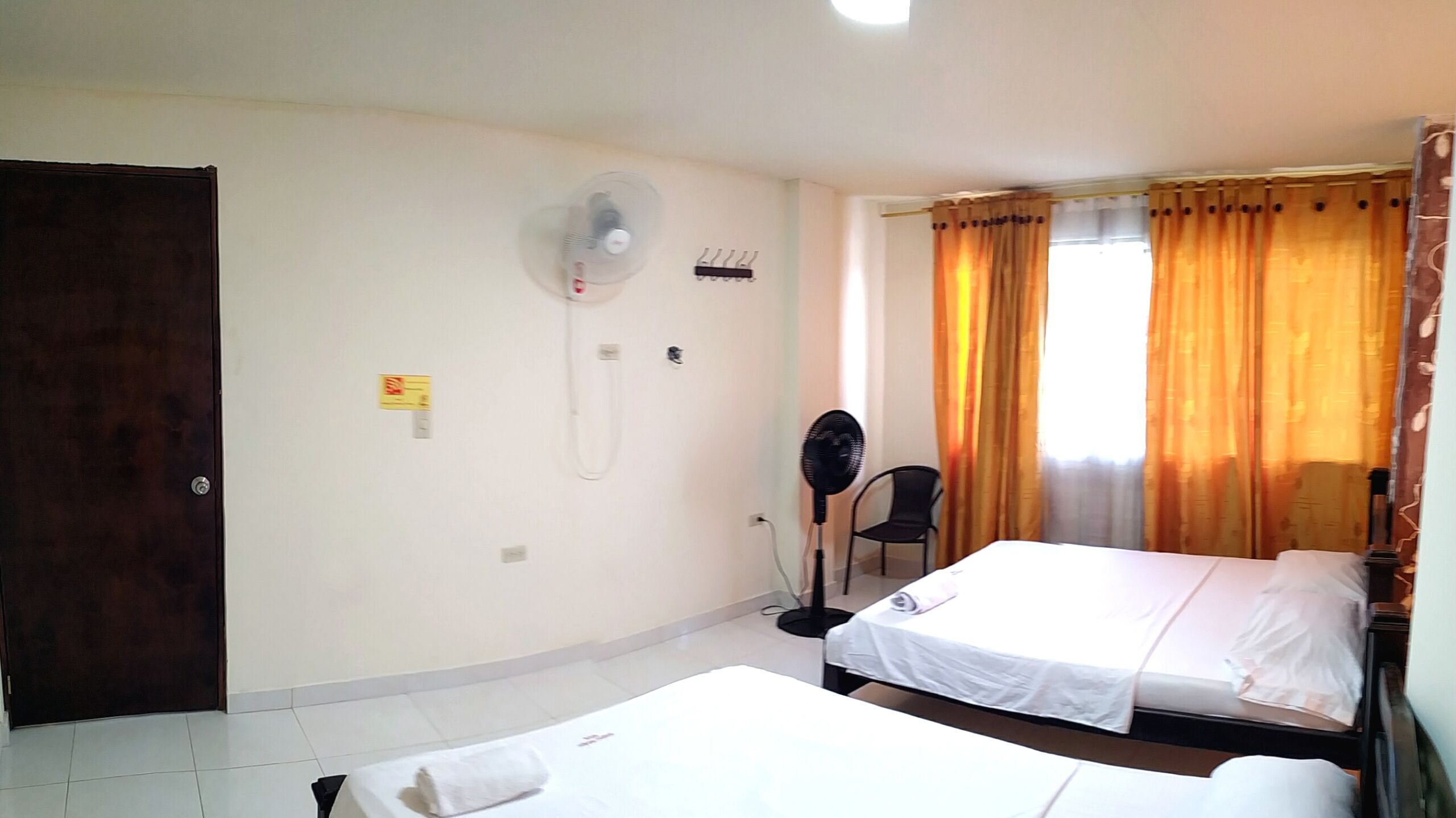 Quarto de hotel com duas camas, um ventilador, secador de cabelo, uma cadeira e uma porta.