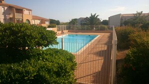 A swimming pool surrounded by a metal fence, with a paved walkway and lush greenery.