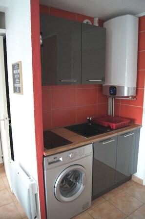 Una cocina compacta con lavadora, un lavamanos y salpicadero de azulejos rojos.