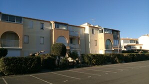 A multi-story residential building with balconies, a parking lot, and a clear sky.