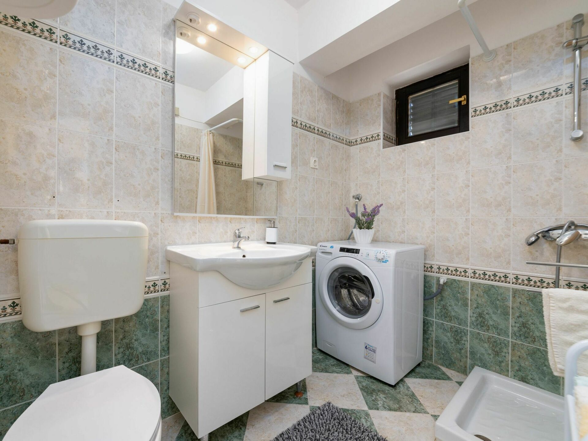 Casa de banho com sanita, lavatório, máquina de lavar roupa e chuveiro.
