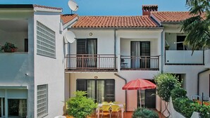 A two-story building with a balcony, a small garden with a table and chairs, and a red umbrella. - Lovely apartment in villa for 5 guests with WIFI, A/C, TV and terrace (Umag)
