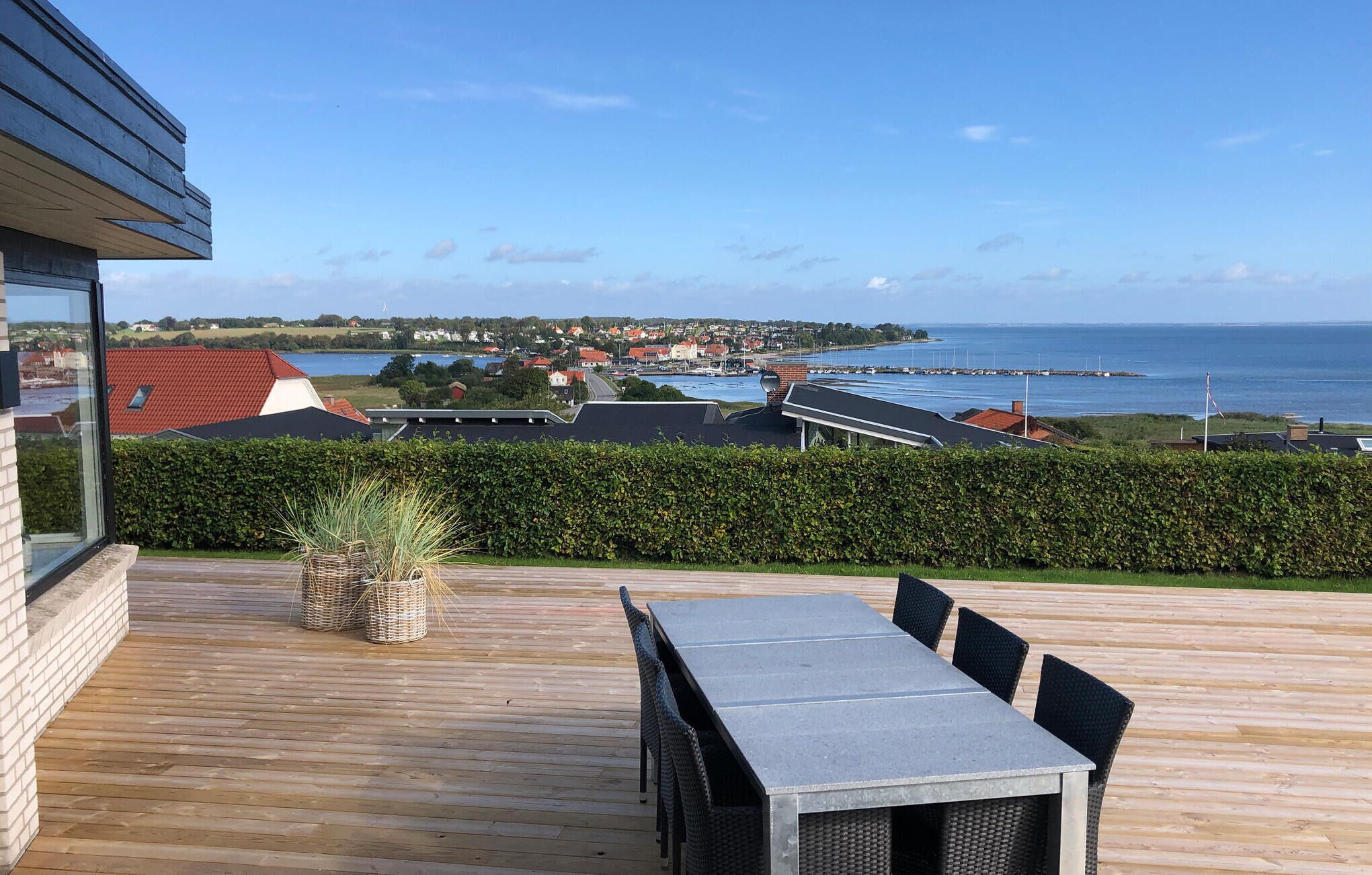 Una terraza de madera con una mesa y sillas, con vistas a un pueblo costero con casas y un puerto deportivo.