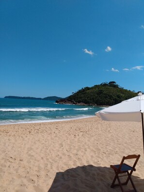 Une plage avec un parasol blanc et une chaise en bois.