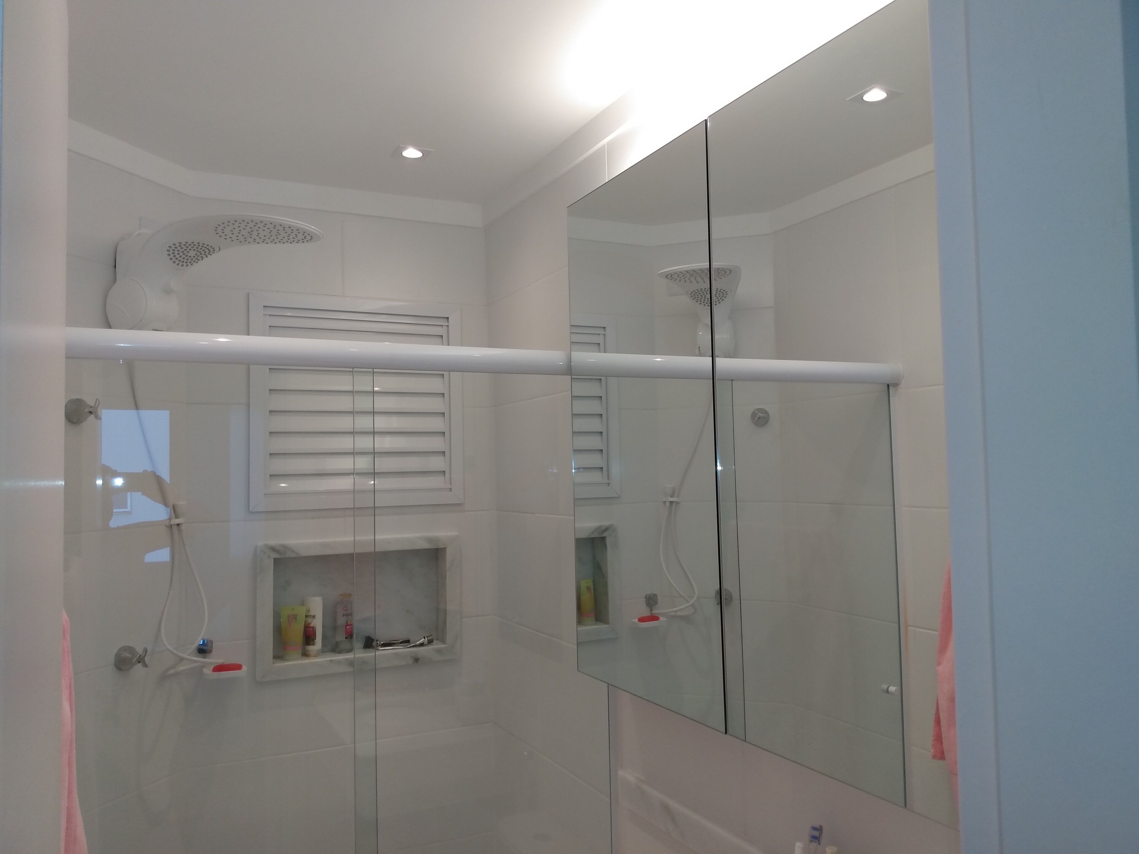 A modern bathroom with a glass shower enclosure, a built-in shelf with toiletries, and a large mirror.