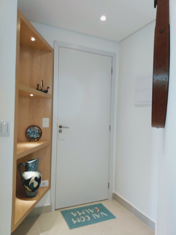 A hallway with a white door, wooden shelving, and a doormat with text. - Apartment in Itaguá, Ubatuba, High Standard, sophistication in family structure. (Itaguá)