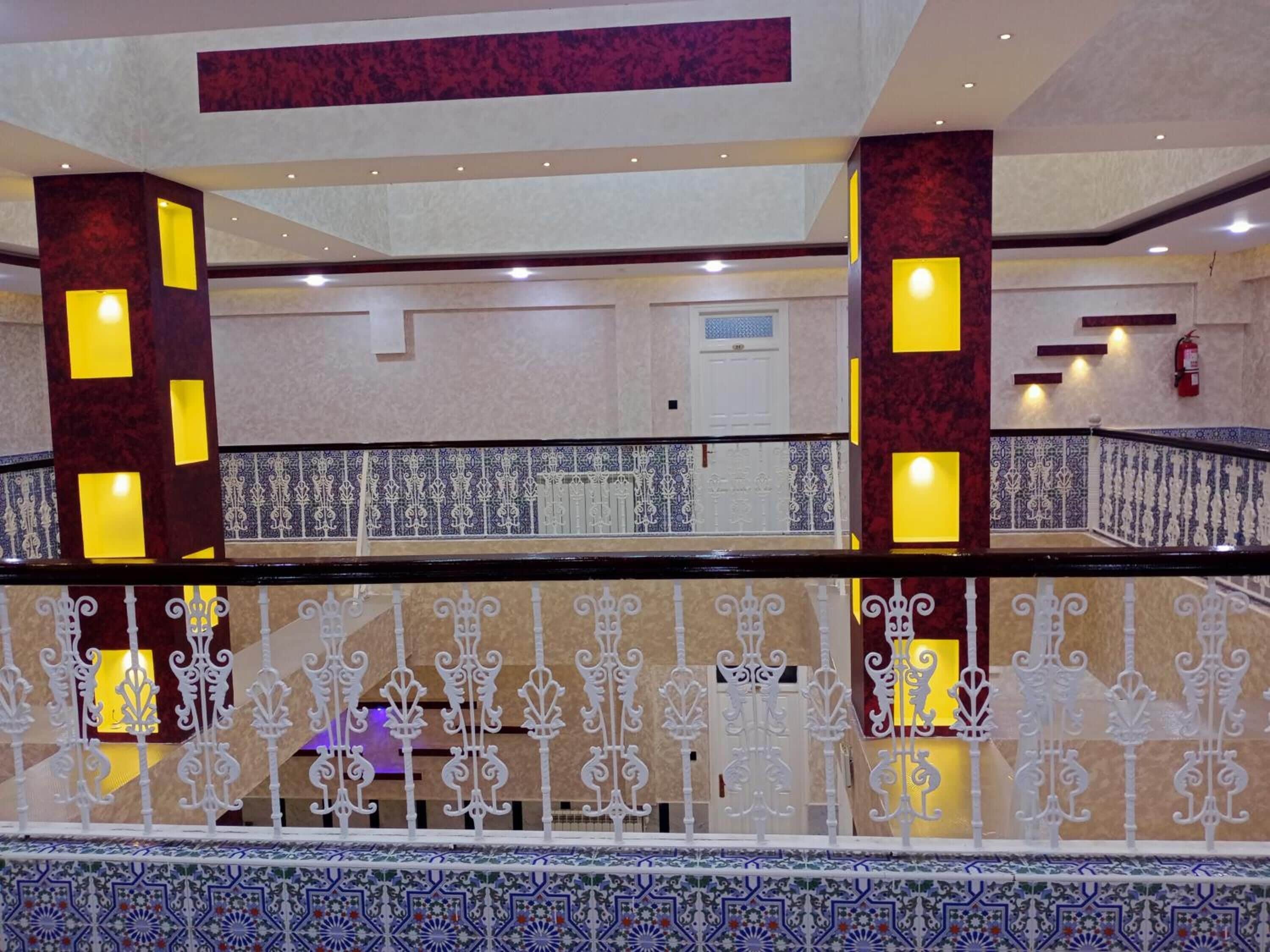 Un hall d’hôtel avec un sol en marbre, une balustrade décorative et un extincteur fixé au mur.