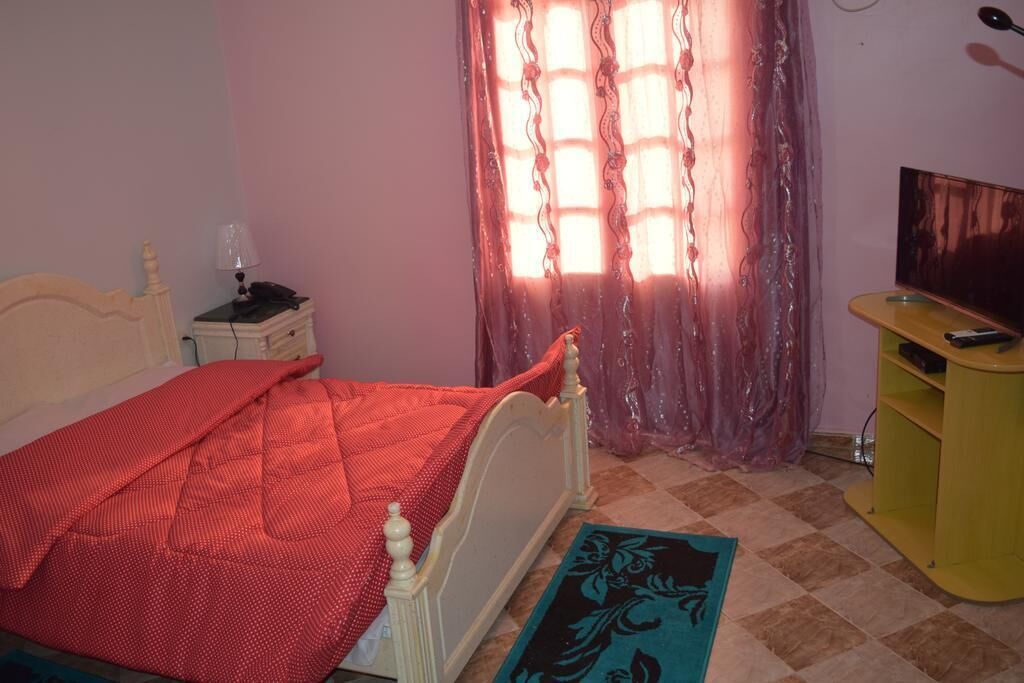 A bedroom with a bed, a nightstand, a TV stand, and a window with curtains.