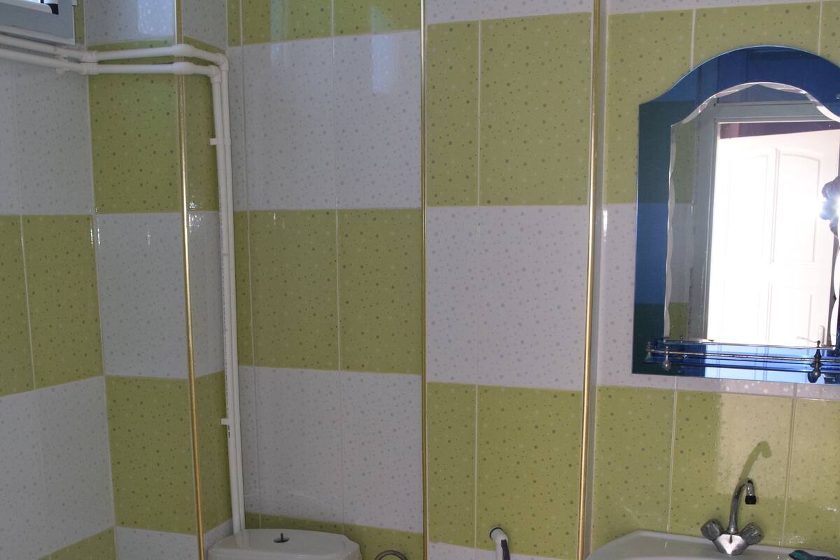 Un baño con inodoro, bidé y lavamanos, con azulejos verdes y blancos.