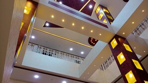 Ein mehrgeschossiges Interieur mit geometrischem Deckenmuster, Einbauleuchten und dekorativen Wandverkleidungen.