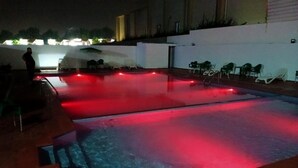 Ein Außenpool mit roter Beleuchtung, umgeben von Stühlen und einer gefliesten Terrasse.