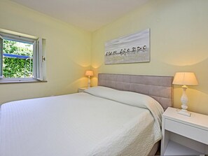 Quarto com cama, duas mesas de cabeceira, janela e um quadro na parede.