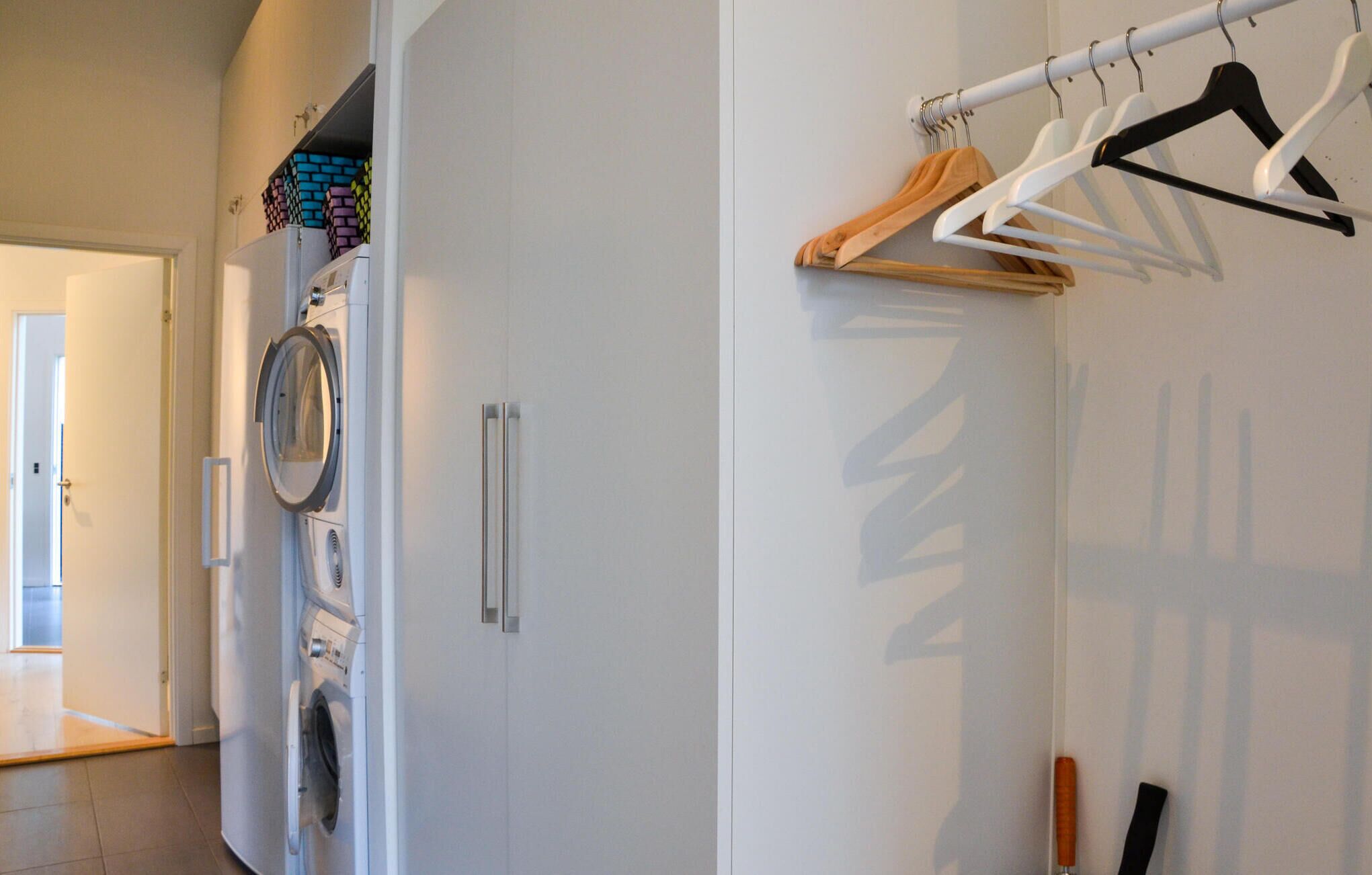 A laundry area with a washing machine, a drying rack, and a door leading to another room.