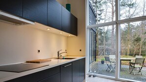 A modern kitchen with dark cabinets, a stainless steel sink, and a large window offering a view of a patio with outdoor furniture. - Amazing home in Græsted with kitchen (Græsted)