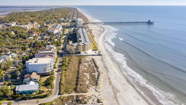 Vista aérea de un pueblo costero con playa, muelle y edificios residenciales.