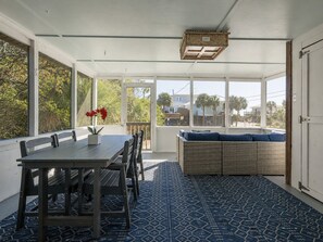 A sunroom with a dining table, chairs, a wicker sofa, and a patterned floor. - Cozy Cottage-Screened Porch-Central Location -Beach Access Across- Pet Considered (Folly Beach)