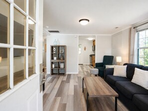 A modern living room with a sofa, coffee table, and a bookshelf. - Cozy Cottage-Screened Porch-Central Location -Beach Access Across- Pet Considered (Folly Beach)