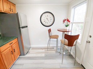 Une cuisine compacte comprenant un réfrigérateur, des placards en bois, une table à manger avec deux chaises et une horloge murale.