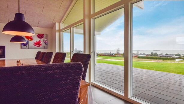Un comedor moderno con una gran mesa y sillas, ventanas amplias que ofrecen vistas a un paisaje verde y una masa de agua.