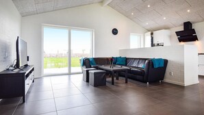 Una sala de estar moderna con un ventanal grande, un sofá, una mesa de centro y un televisor sobre un mueble.