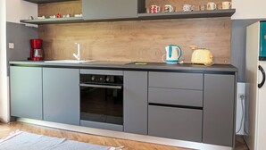 A modern kitchen with grey cabinetry, a built-in oven, a coffee maker, a kettle, and a toaster.