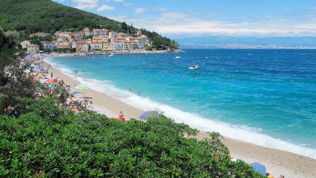 A coastal town with a beach, clear blue waters, and buildings along the shore.