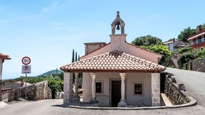 A small building with a bell tower, a no parking sign, and a clear view of the sea.