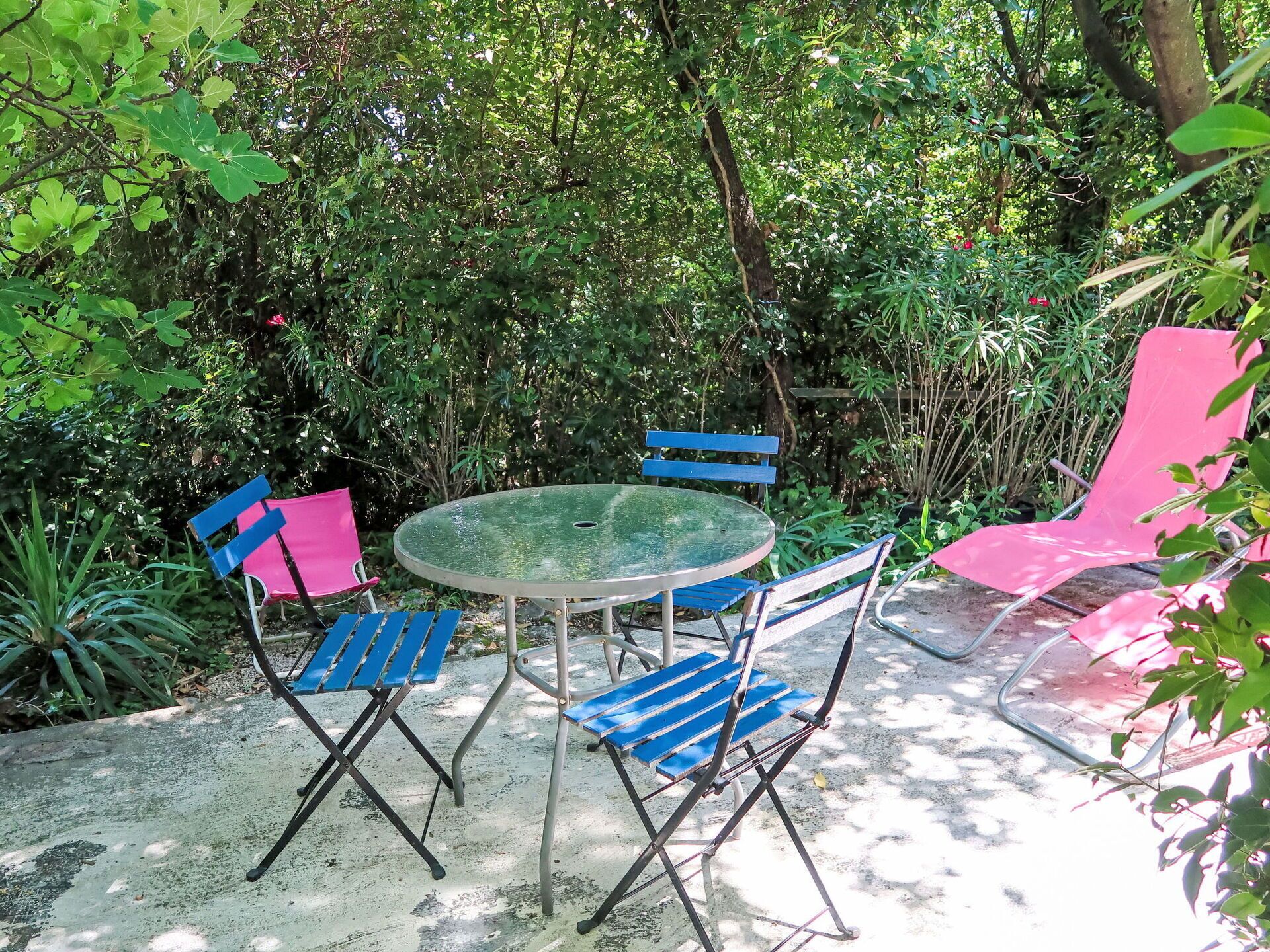 Una mesa redonda con cuatro sillas azules y una silla roja en un jardín.