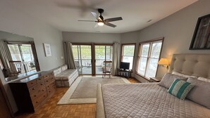 A spacious bedroom with a large bed, a dresser, a ceiling fan, and a view of the outdoors through the sliding glass doors.