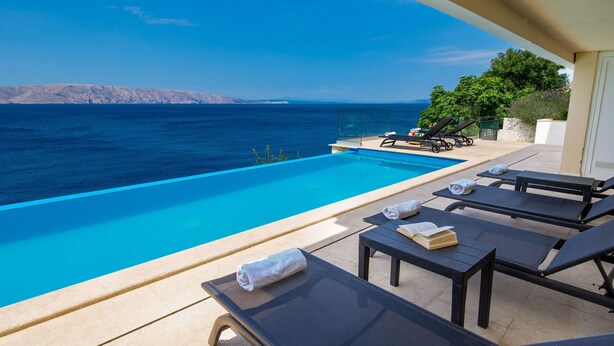 Un espace aménagé au bord de la piscine, avec des chaises longues et une vue sur la mer.
