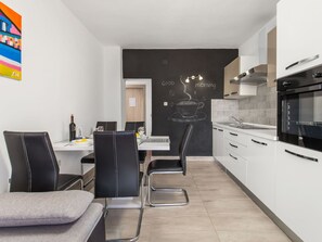 Une cuisine moderne avec des meubles blancs, une cuisinière noire et un coin repas comprenant deux chaises et une table.