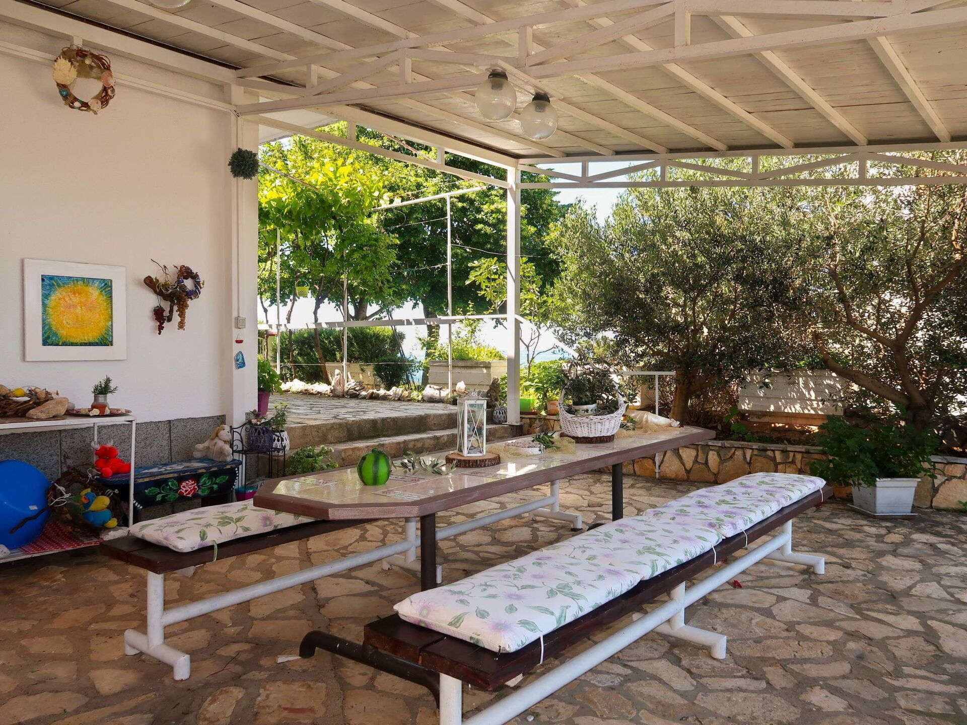 An outdoor patio with stone flooring, two benches, a table, and potted plants.