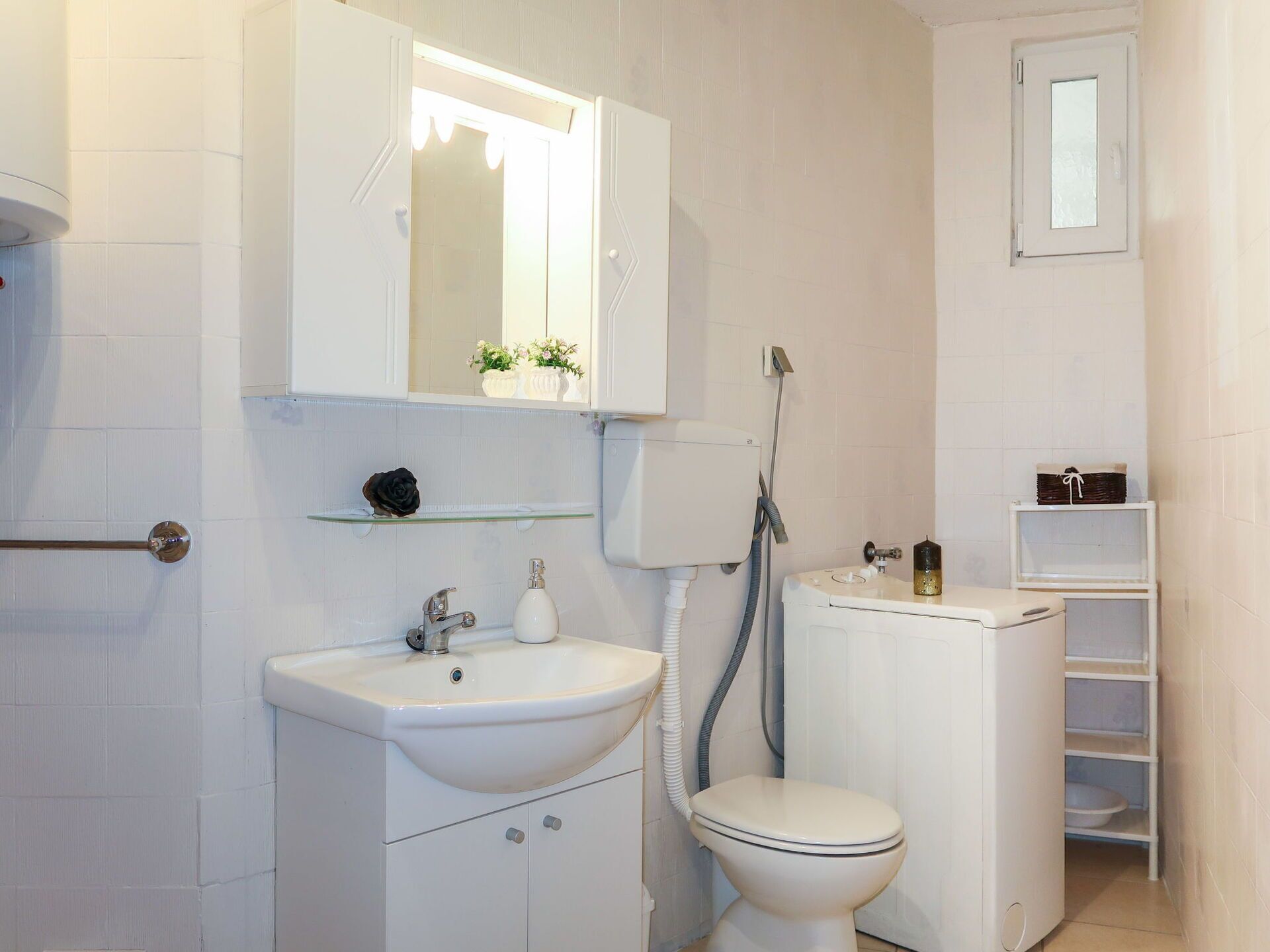 A bathroom with a white sink, toilet, and shower. There is a mirror above the sink and a shelf with decorative items.