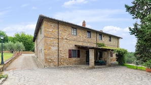 A stone building with a covered porch, a gravel driveway, and surrounding greenery. - Cozy home in Tavarnelle Val di Pesa with WiFi (Tavarnelle Val di Pesa)