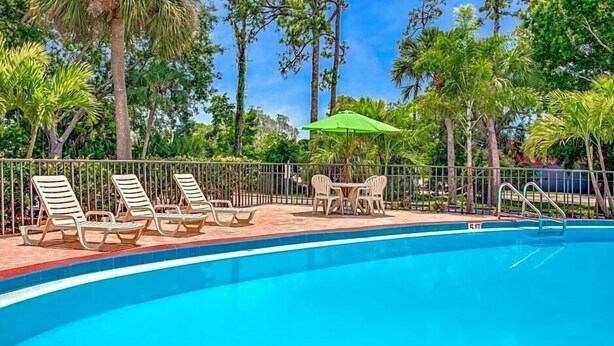 Zona de piscina con sillones de descanso y una mesa con sombrilla.